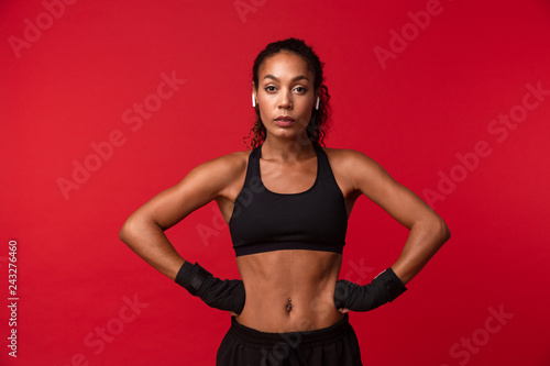 Portrait of african american woman 20s in black sportswear standing with sports bandages on her hands, isolated over red background