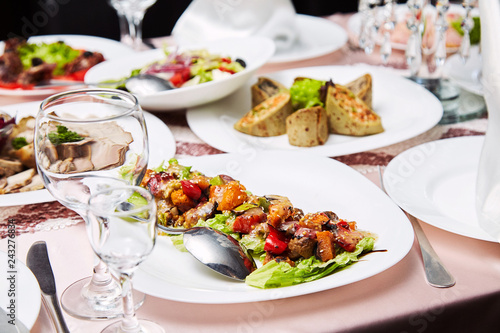 Fresh salad with tomatoes and meat. Delicious prepared and decorated food on table in restaurant. Restaurant table setting decor with glasses. Catering table