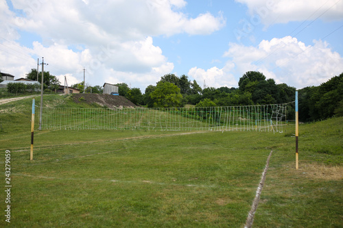 Old volleyball net in the village. Games for poor children outdoors. Summer sport field near the forest.