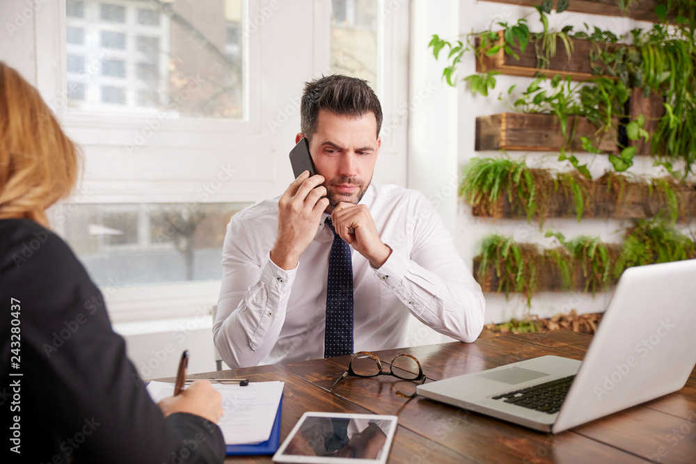 Portrait of businessman sitting at office desk in front of laptop and making a call while working on new business. Portrait of businessman sitting at office desk in front of laptop and making a call while working on new business.