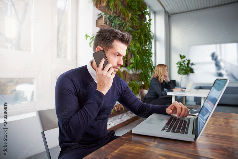 Businessman with making a call and working on laptop while sitting in the office Businessman with making a call and working on laptop while sitting in the office