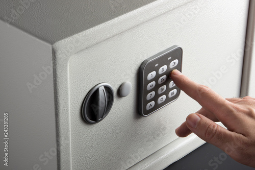 the hand opens a combination lock on the safe, a light safe on a dark background photo