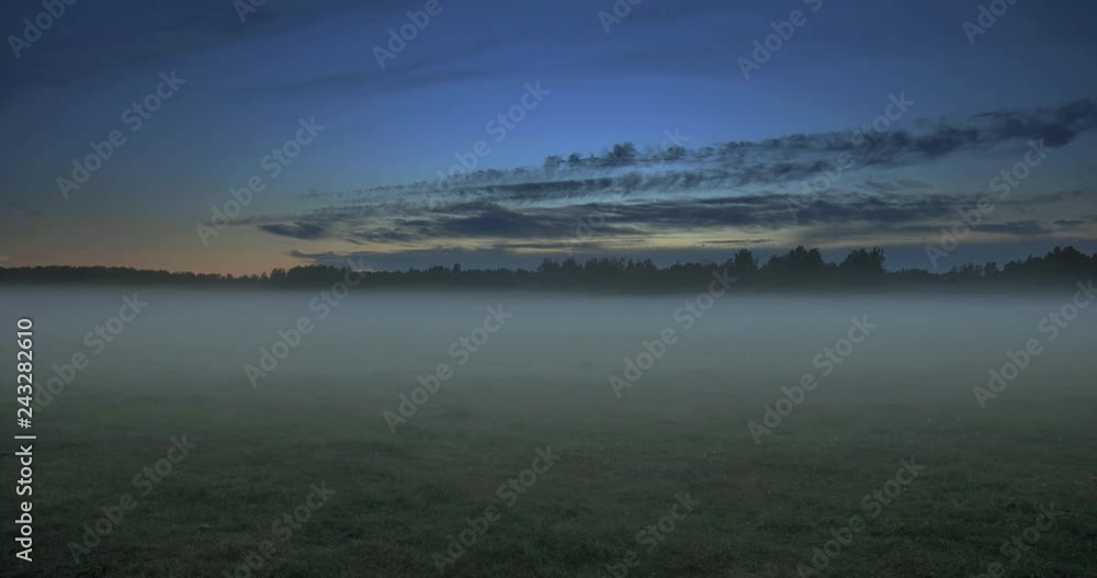 Time lapse of clouds moving above a field with fog flowing through with trees in the background Time lapse of clouds moving above a field with fog flowing through with trees in the background