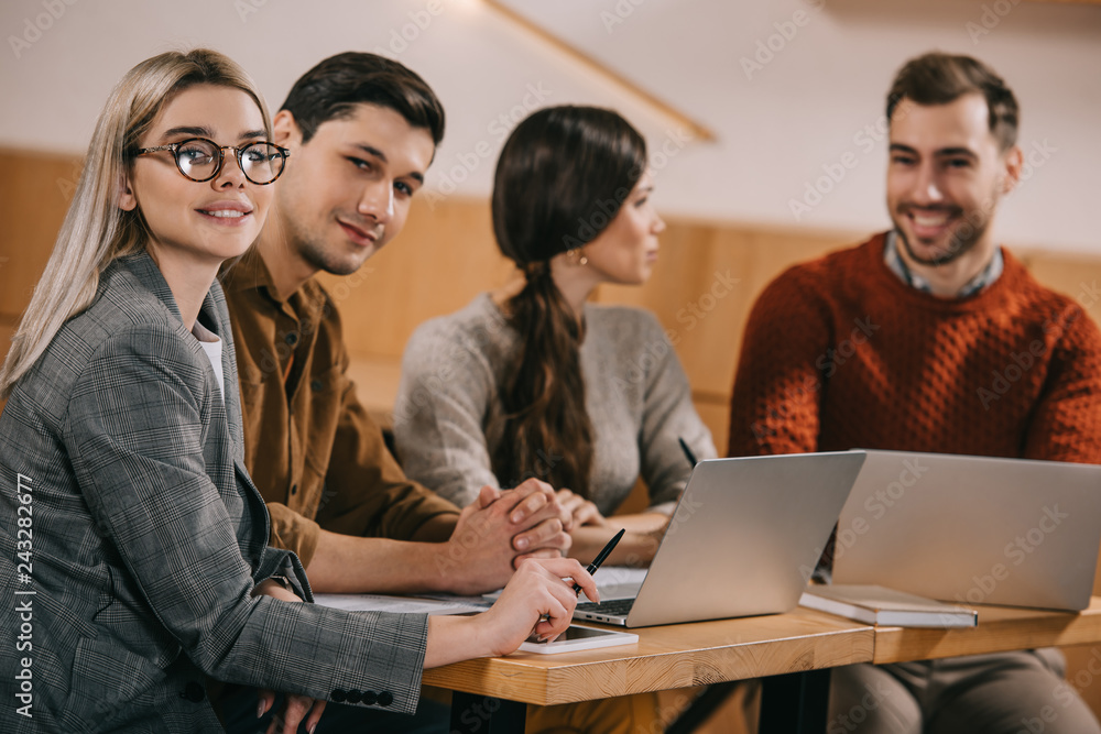 selective focus of woman in glasses and handsome man sitting in cafe with coworkers on background selective focus of woman in glasses and handsome man sitting in cafe with coworkers on background