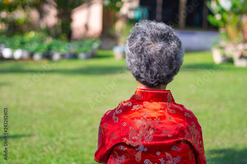 Back view of senior woman wearing Cheongsam red shirt sitting in garden.