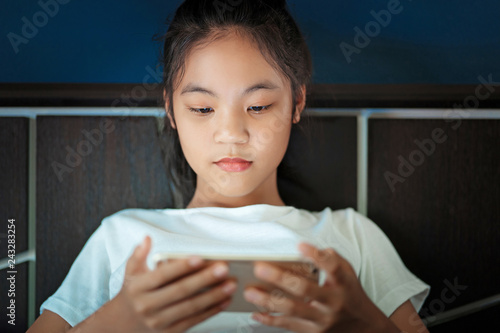 teenage girl sitting in bed  playing a smartphone in social internet  in the dark light under the blacket. The blue light has a negative effect on the child's eyes. photo