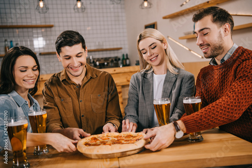 cheerful friends smiling while taking pieces of tasty pizza in bar