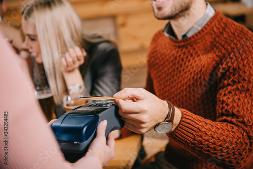 cropped view of female cashier holding terminal while man paying by credit card in cafe