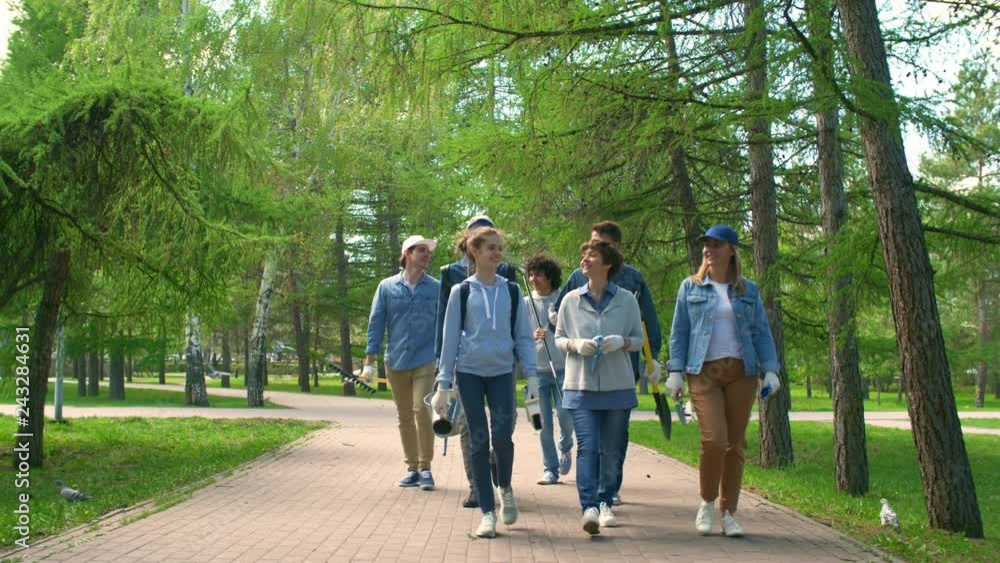 Wide shot of several people with special stuff going home after cleaning park area Wide shot of several people with special stuff going home after cleaning park area