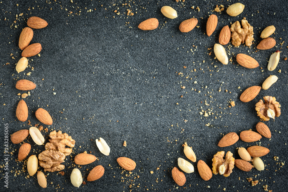 Fototapeta premium Nuts background of almonds, peanuts and walnuts with crumbs on black background.