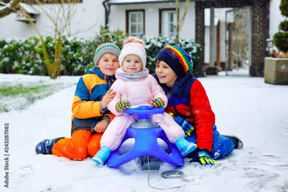 Two little kid boys and cute toddler girl sitting together on sledge. Siblings, brothers and baby sister enjoying sleigh ride during snowfall. Children sledding on snow. Active fun for family vacation
