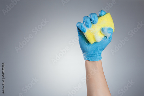 Hand in blue glove holding a yellow sponge on gray background