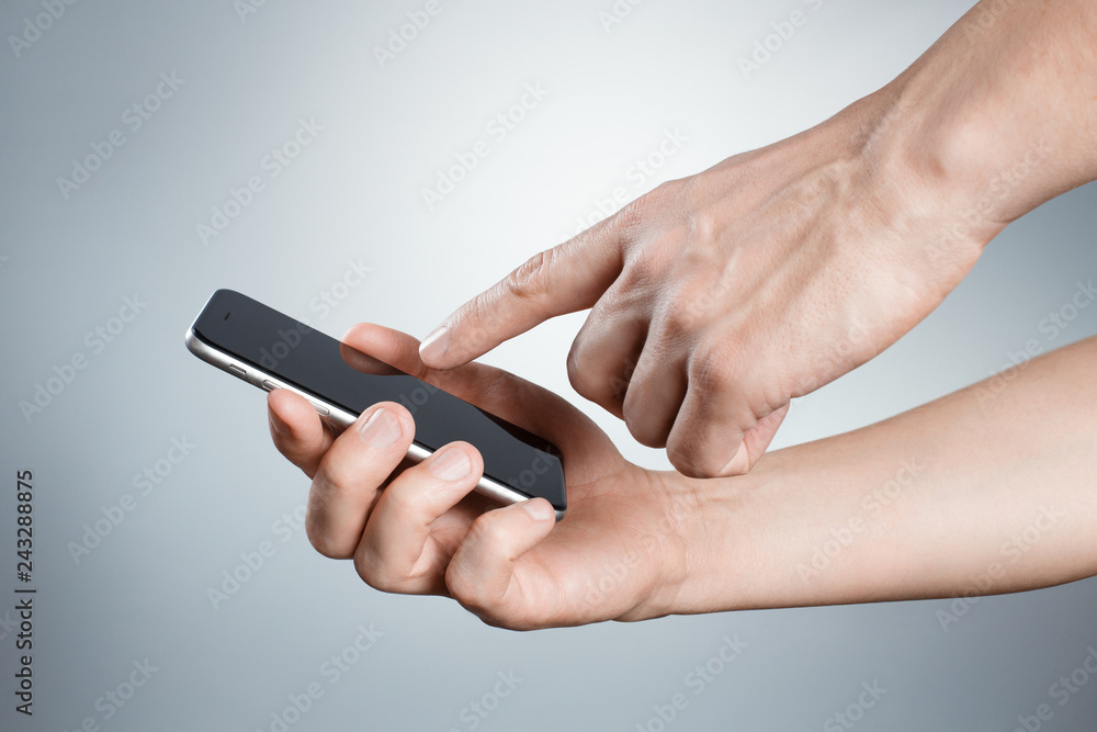 Hands holding and touching black smartphone on gray background Hands holding and touching black smartphone on gray background