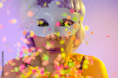 Fototapeta Naklejka Na Ścianę i Meble -  Blowing Confetti. Portrait of latin woman wearing purple wig and makeup mask. Colorful background. Carnival concept, fun and party.