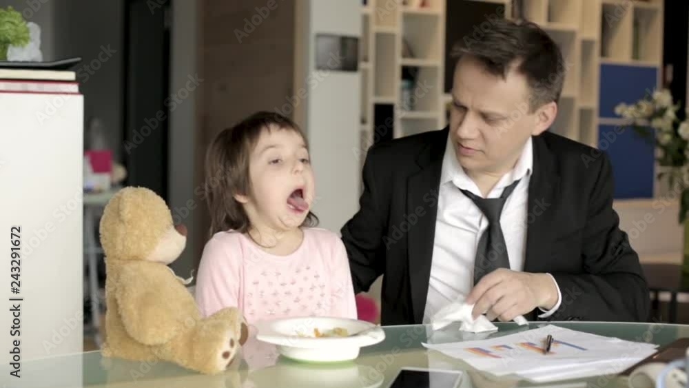Father in suit working with papers and feeding daughter Father in suit working with papers and feeding daughter