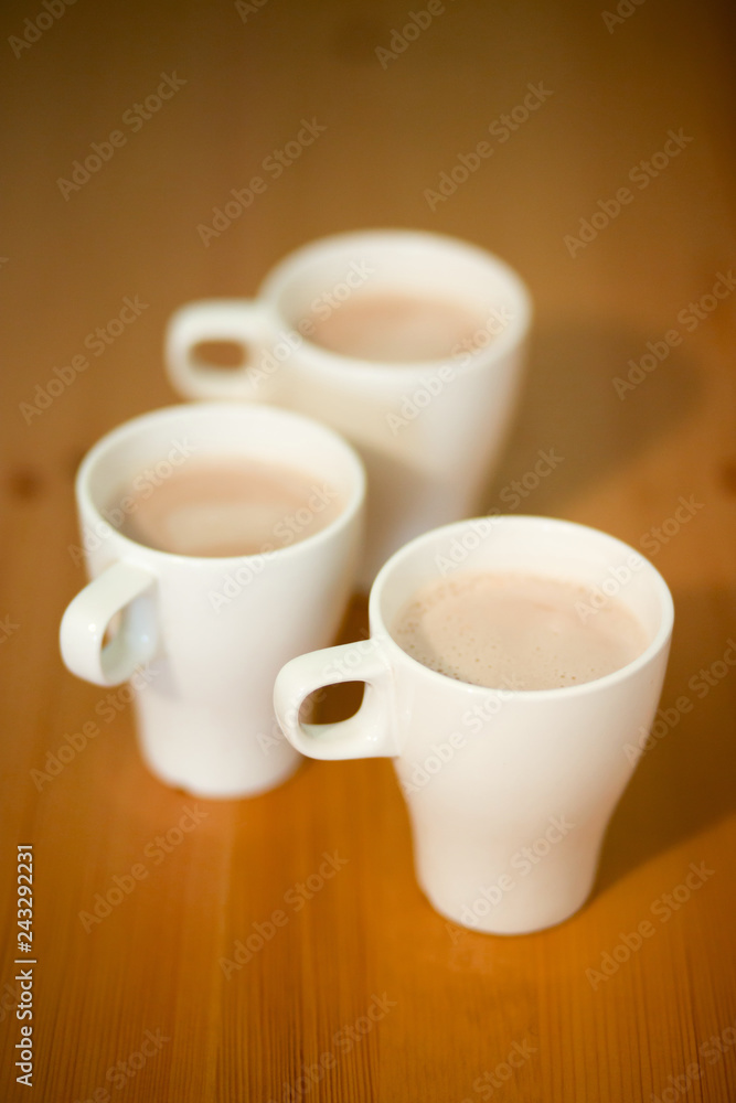 Three white cups of coffee, cocoa or latte on a wooden background on the table, close-up Three white cups of coffee, cocoa or latte on a wooden background on the table, close-up