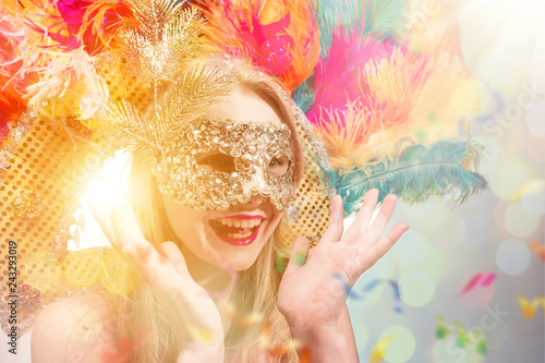 Fototapeta Naklejka Na Ścianę i Meble -  Beautiful young woman in carnival mask. Beauty model woman wearing masquerade mask at party over holiday background with magic glow. Christmas and New Year celebration. Glamour lady with perfect make