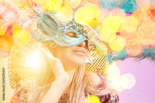 Beautiful young woman in carnival mask. Beauty model woman wearing masquerade mask at party over holiday background with magic glow. Christmas and New Year celebration. Glamour lady with perfect make