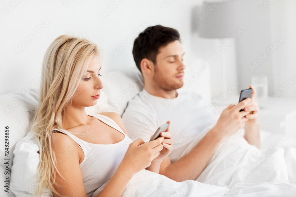 people, technology, internet addiction and communication concept - couple with smartphones in bed people, technology, internet addiction and communication concept - couple with smartphones in bed