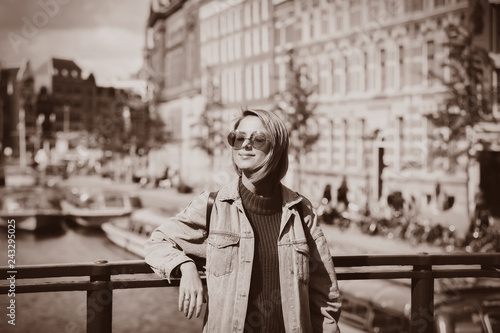 Young girl in sweater and orange sunglasses at bridge in Amsterdam street. Holland, Netherlands. Autumn season Image in sepia color style