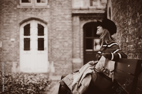 Young girl in hat sitting at bench in Bruges, Belgium. Autumn season. Image in sepia color style