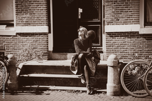 Photography Young girl in sunglasses and sweater with backpack sitting at street in Amsterdam