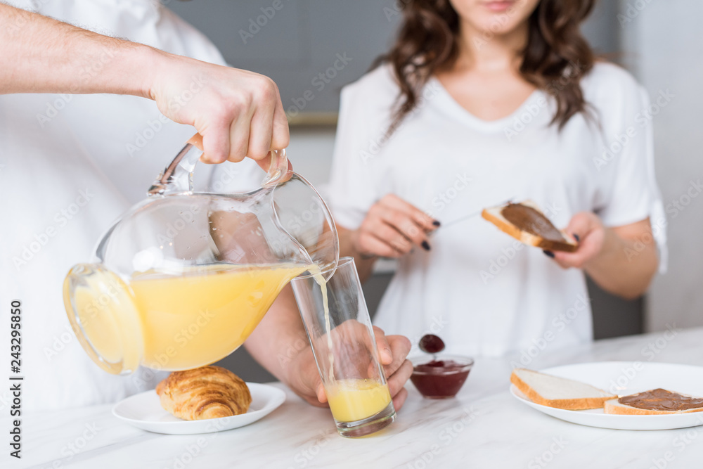 selective focus of man pouring orange juice in glass near girlfriend in kitchen