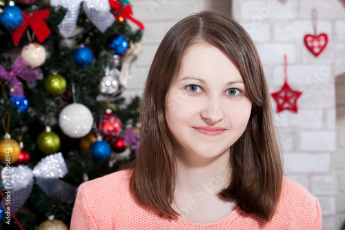 Happy young lady with gifts by the fireplace near Christmas tree