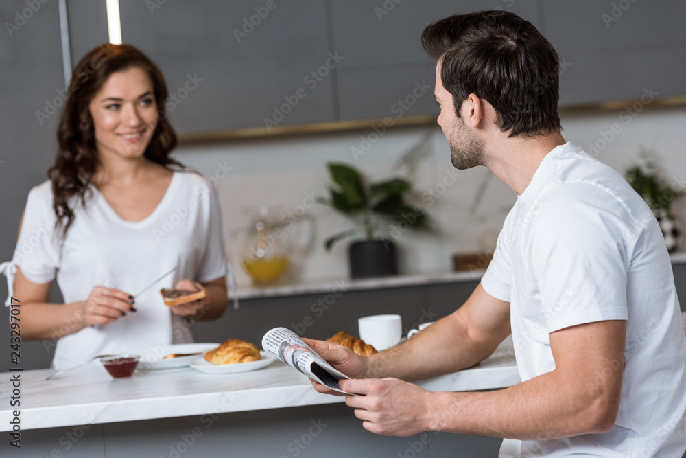selective focus of man holding newspaper and looking at woman in kitchen