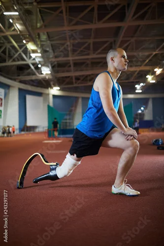 Obraz Active sportsman with prosthesis in right leg doing stretching exercise at stadium before paralympic competition