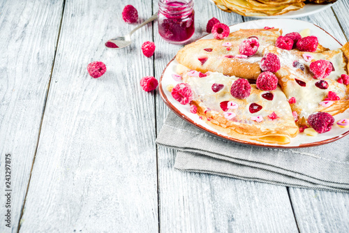 Idea for Valentine's Day surprise gift. Cute pancakes crepes with berry sauce and heart shaped cutouts. Romantic valentine breakfast. On wooden table, with fresh raspberries. Copy space