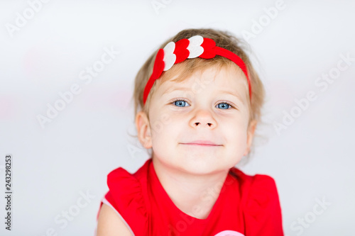 Little blonde girl in red dress with red wreath with heatrs on the white background with pink hearts on the St. Valentine's day photo