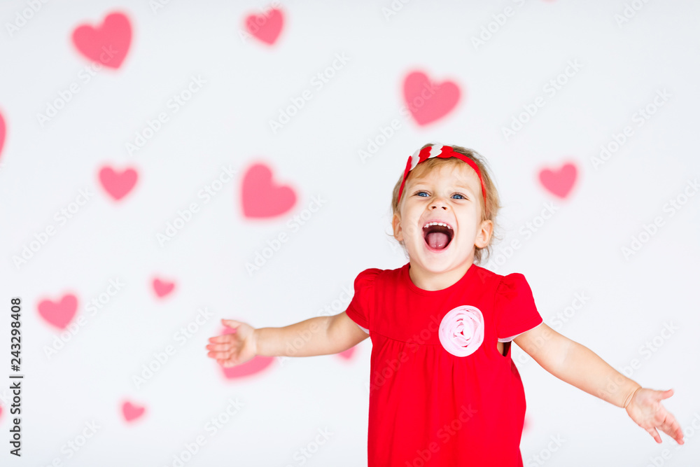 Little blonde girl in red dress with red wreath with heatrs on the white background with pink hearts on the St. Valentine's day