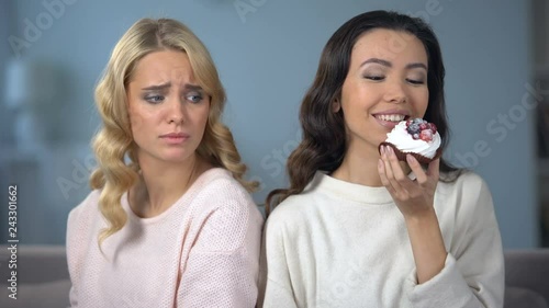 Hungry woman on diet looking at her skinny friend enjoying tasty cake, envy photo