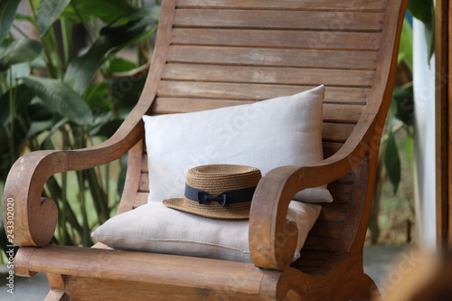 On the porch near the door there is a wooden armchair with pillows on which lies a hat. photo