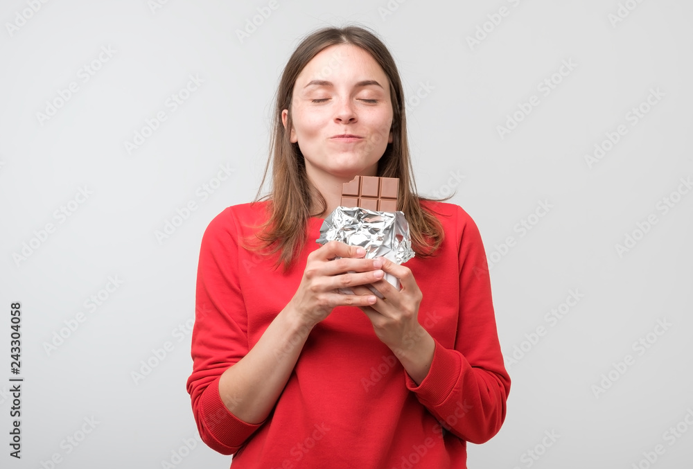 European young lady standing over white background while biting chocolate. European young lady standing over white background while biting chocolate.
