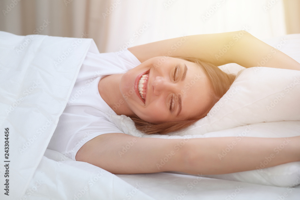 Beautiful young and happy woman sleeping while lying in bed comfortably and blissfully smiling Beautiful young and happy woman sleeping while lying in bed comfortably and blissfully smiling