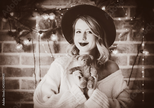 Portrait of a young cozy woman in white sweater with teddy beartoy and Christmas lights on background. photo