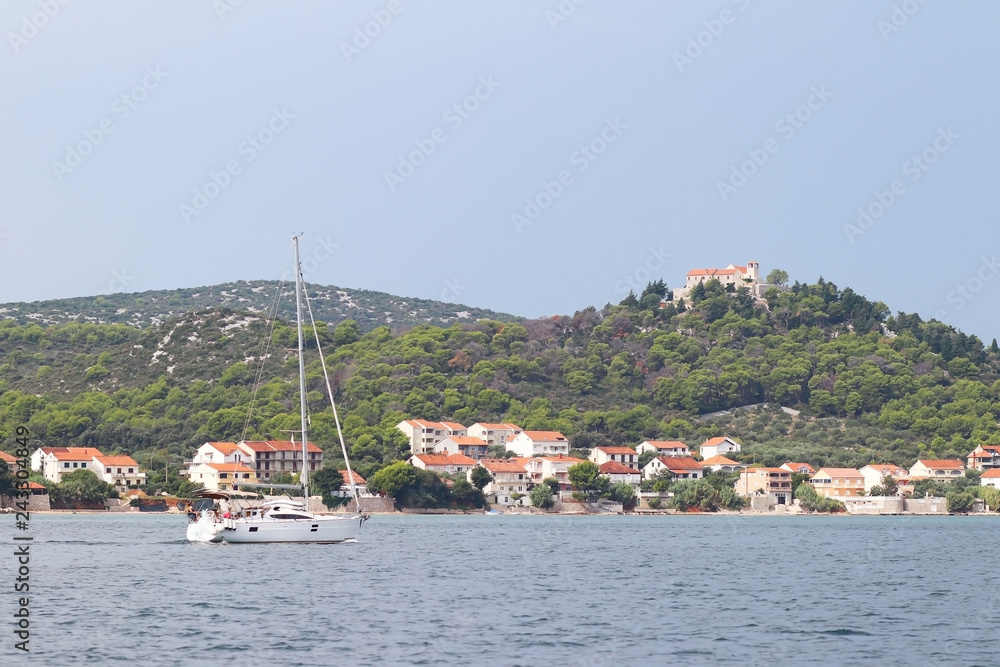 Pasman, Croatia, Europe - 7 9 2018: Embankment of a small Croatian town in the Adriatic Sea. Sailing yacht on the background of the Dalmatian Riviera. Tourism and architecture of the Mediterranean.