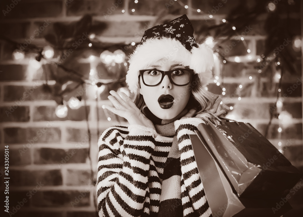 Obraz premium Portrait of a young cozy woman with shopping bags and Christmas lights and pine branch on background.