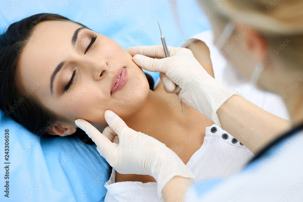 Young female patient visiting dentist office.Beautiful woman with healthy straight white teeth sitting at dental chair with open mouth during oral checkup while doctor working at teeth Young female patient visiting dentist office.Beautiful woman with healthy straight white teeth sitting at dental chair with open mouth during oral checkup while doctor working at teeth