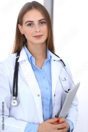 Doctor woman using tablet computer while standing straight near window in hospital. Happy physician at work. Medicine and health care concept photo