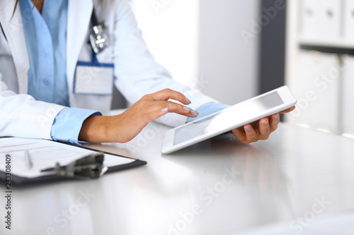 Unknown doctor woman using tablet computer while standing straight near window in hospital, close-up of hands. Medicine and health care concept