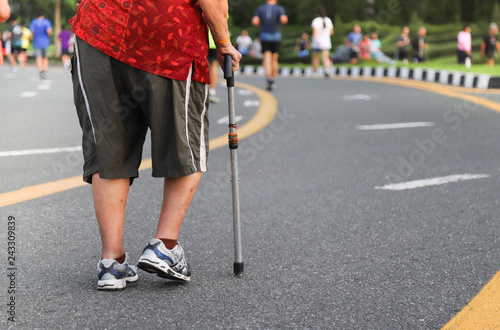 Closeup of elderly disabled Asian woman walking with walking stick in walking track. Rehabilitation by herself. 