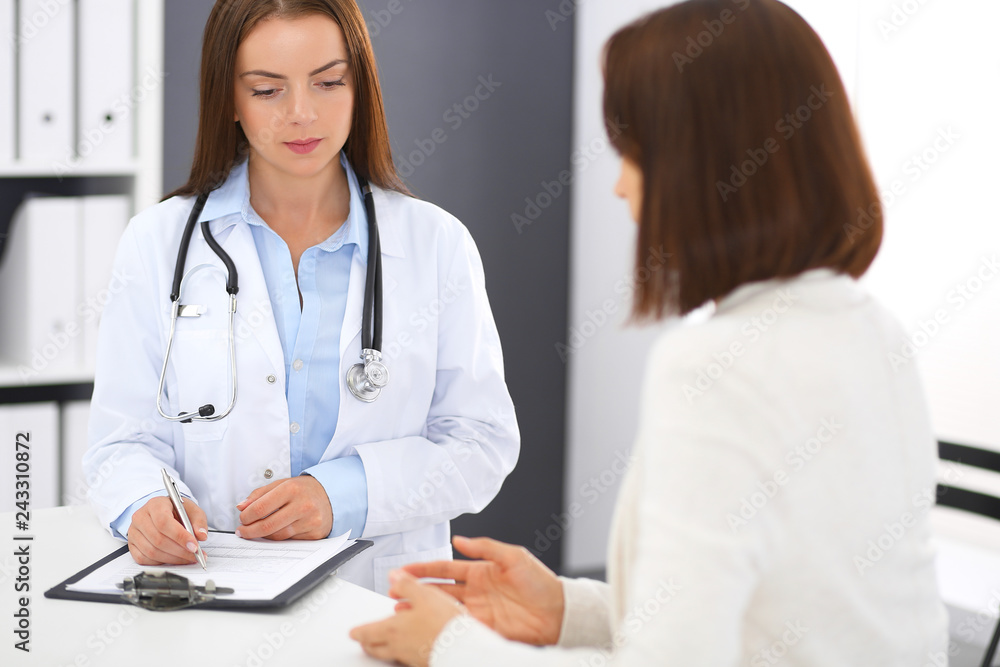 Doctor and patient discussing something while standing near reception desk in emergency hospital. Physician at work in clinic. Medicine and health care concept Doctor and patient discussing something while standing near reception desk in emergency hospital. Physician at work in clinic. Medicine and health care concept