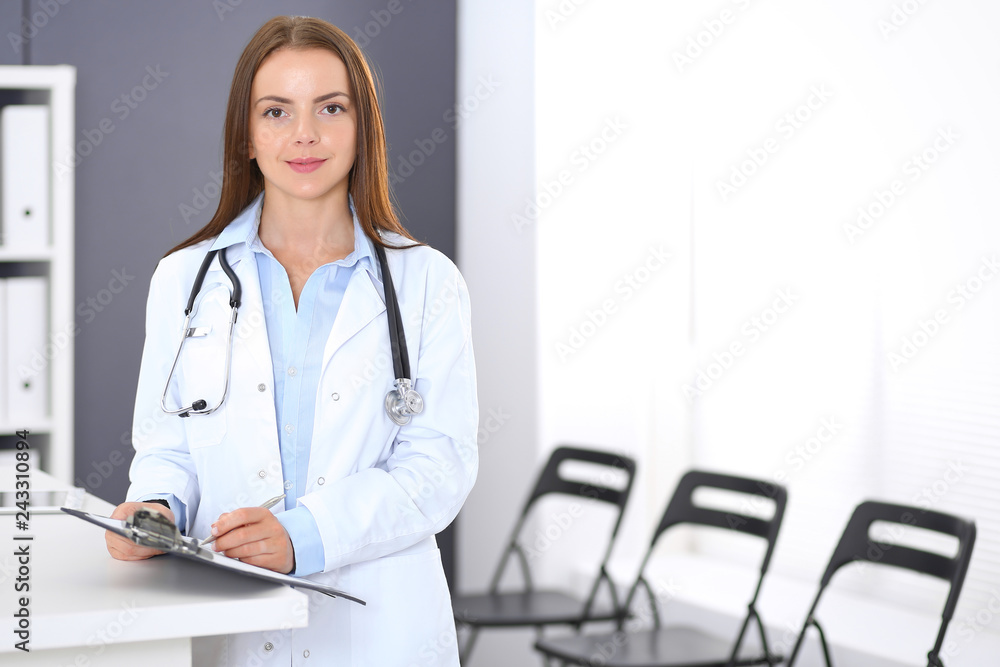 Doctor woman at work. Portrait of female physician standing near reception desk at clinic or emergency hospital. Medicine and healthcare concept Doctor woman at work. Portrait of female physician standing near reception desk at clinic or emergency hospital. Medicine and healthcare concept