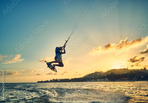 Young man kite boarder jumps over the sea at sunset
