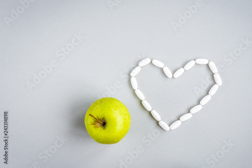 Pills in shape of heart with green apple on gray background. 