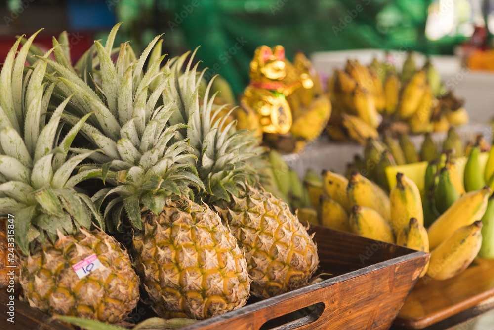 Group of pine apple put in the basket, some have price stick on it and have bananas and golden cat toy in background