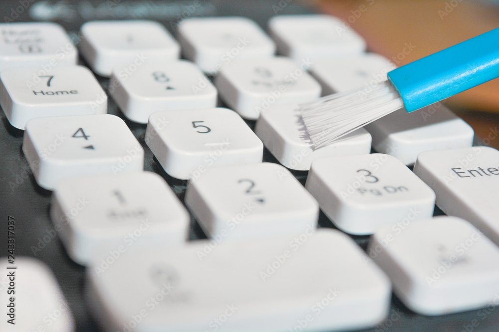 Closeup photo of cleaning the keyboard with white keys with a blue brush Closeup photo of cleaning the keyboard with white keys with a blue brush